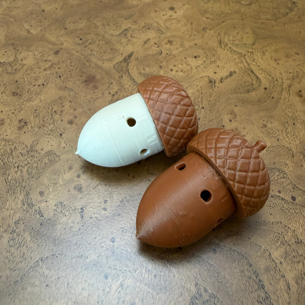 Two acorn-shaped scent work hides, one brown and one white, placed on a textured brown wood surface.