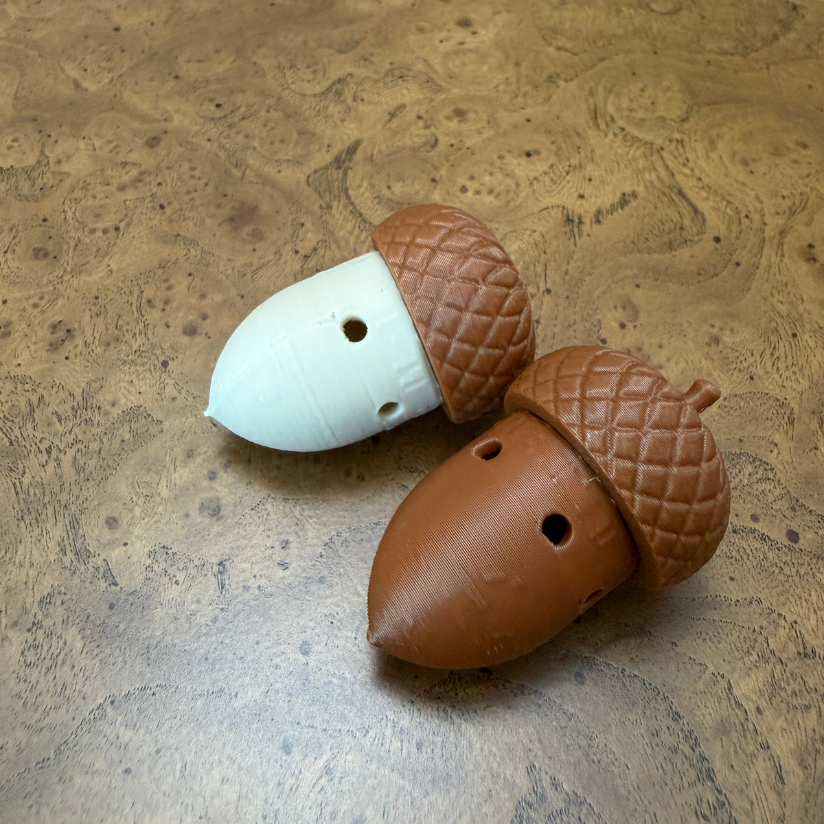 Two acorn-shaped scent work hides, one brown and one white, placed on a textured brown wood surface.