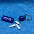 A small blue metal keychain container shown open, with three white cotton swabs placed in front. The main body has the word "Birch" printed in white.