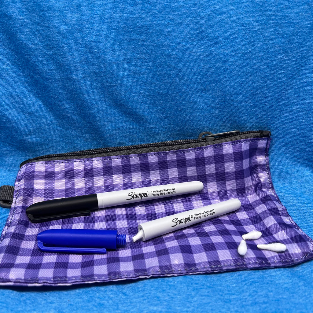 A purple and white gingham fabric pouch with a black zipper, shown on a blue textured background. Two Sharpie marker hides are placed on the pouch, along with three white cotton swabs.  One of the hides is open with a Q-Tip partially out. 