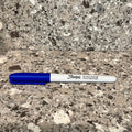 A blue and white Sharpie marker shaped scent work hide lying on a speckled stone countertop with a matching stone backsplash behind it.