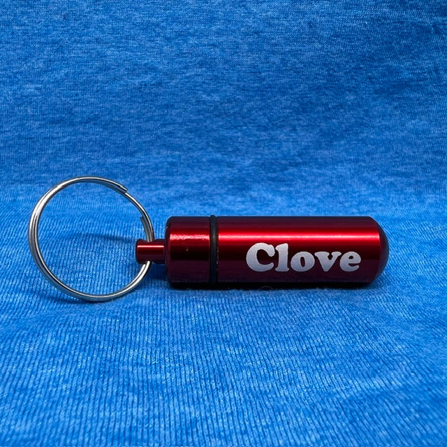 A red cylindrical metal keychain tool with the word 'Clove' printed in white, attached to a silver split ring, photographed on a textured blue fabric background.