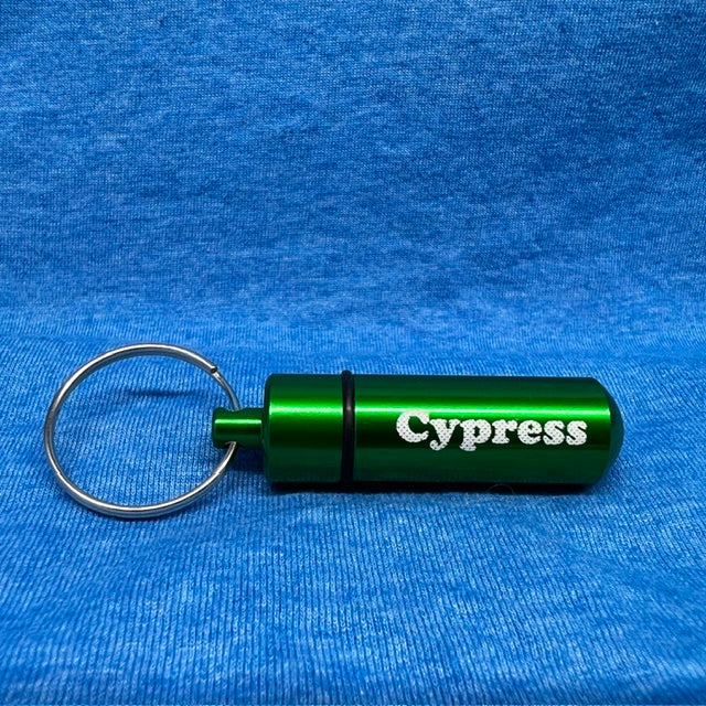 A green anodized aluminum keychain bottle with the word 'Cypress' printed in white, attached to a silver metal key ring, resting on a textured blue fabric background.