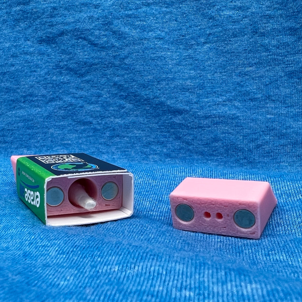 The eraser scent work hide shown opened.  From this angle you can see the magnets used to hold the hide closed as well as the chamber for adding odor.  A Q-tip head is inside the chamber demonstrating size. 